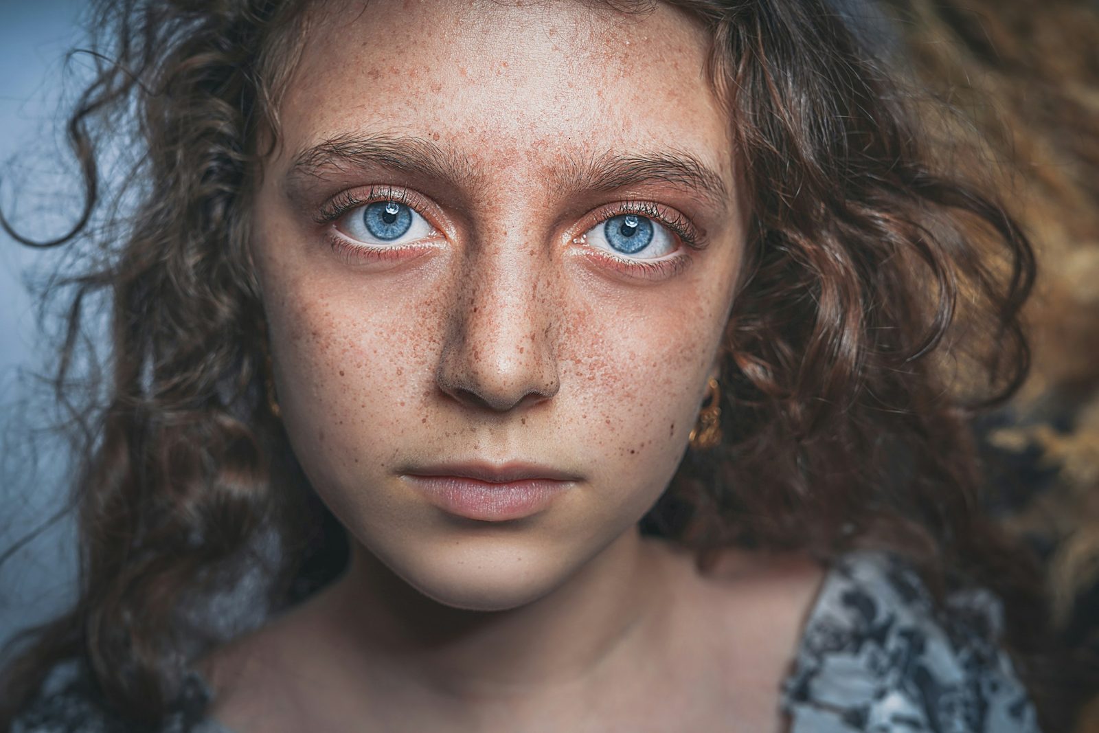 A close portrait of a freckled face with blue eyes that fills the frame with her face