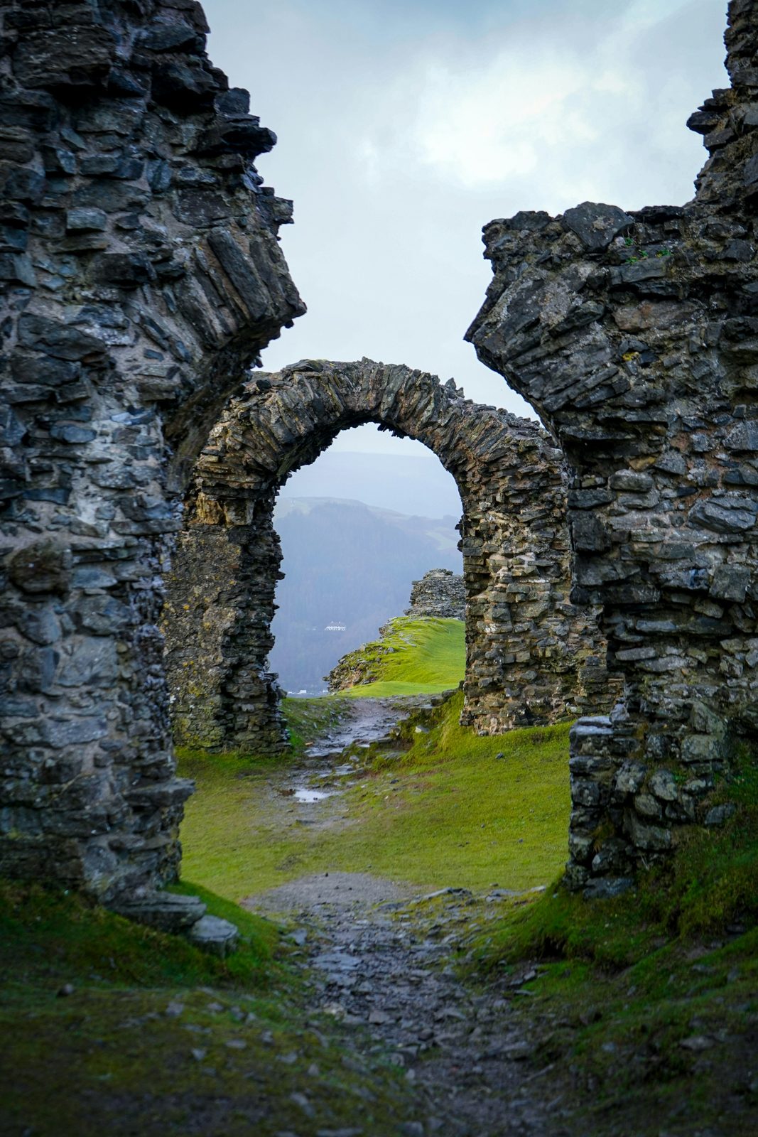 A green valley and mountains seen through a ruined stone arch