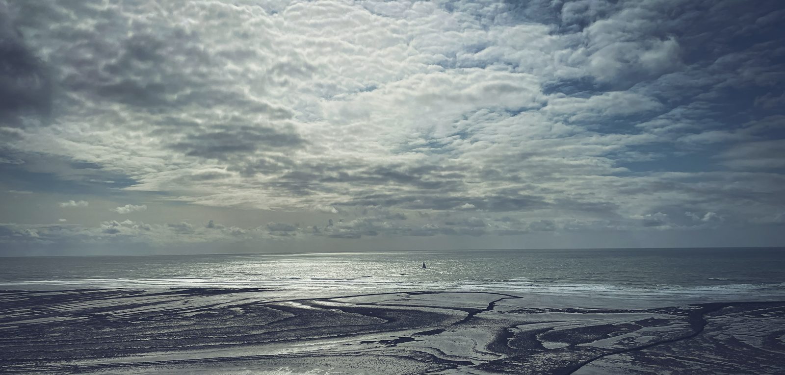Tidal flats under a large cloudy sky, with the horizon on the lower third line