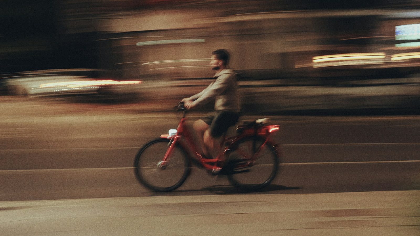 A cyclist panned at night: the rider soft but readable against a streaked street