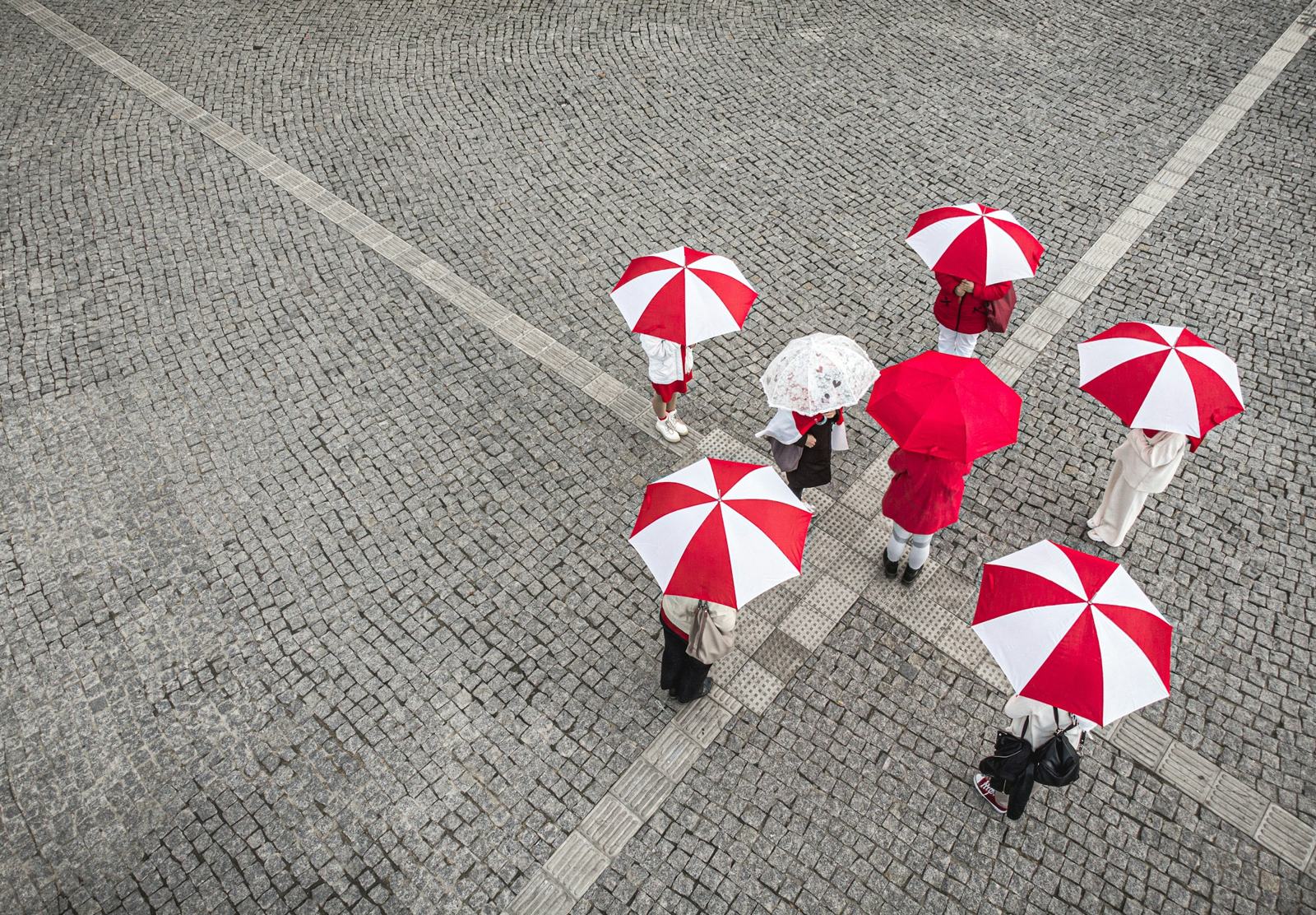 Red-and-white striped umbrellas seen from above, broken by one plain red umbrella and one white one