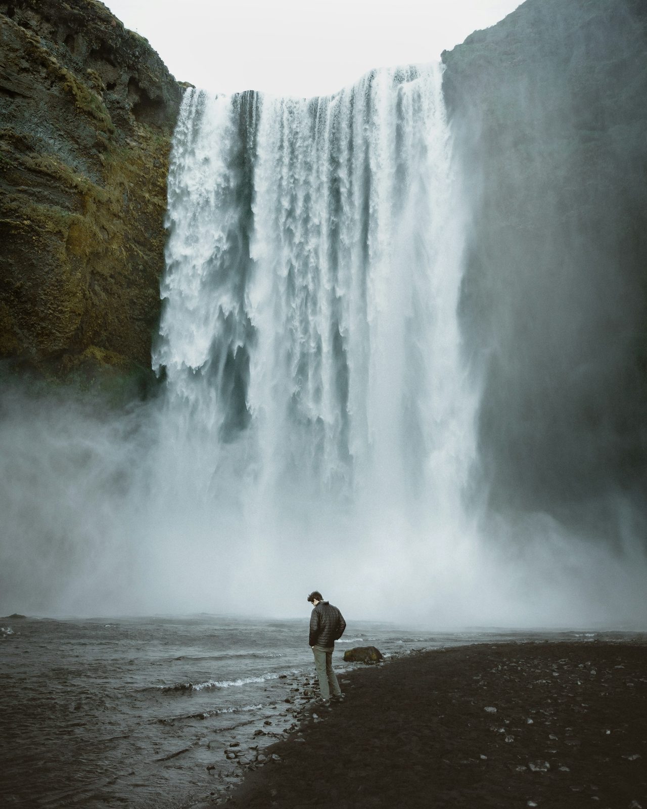 A small figure in front of a huge waterfall