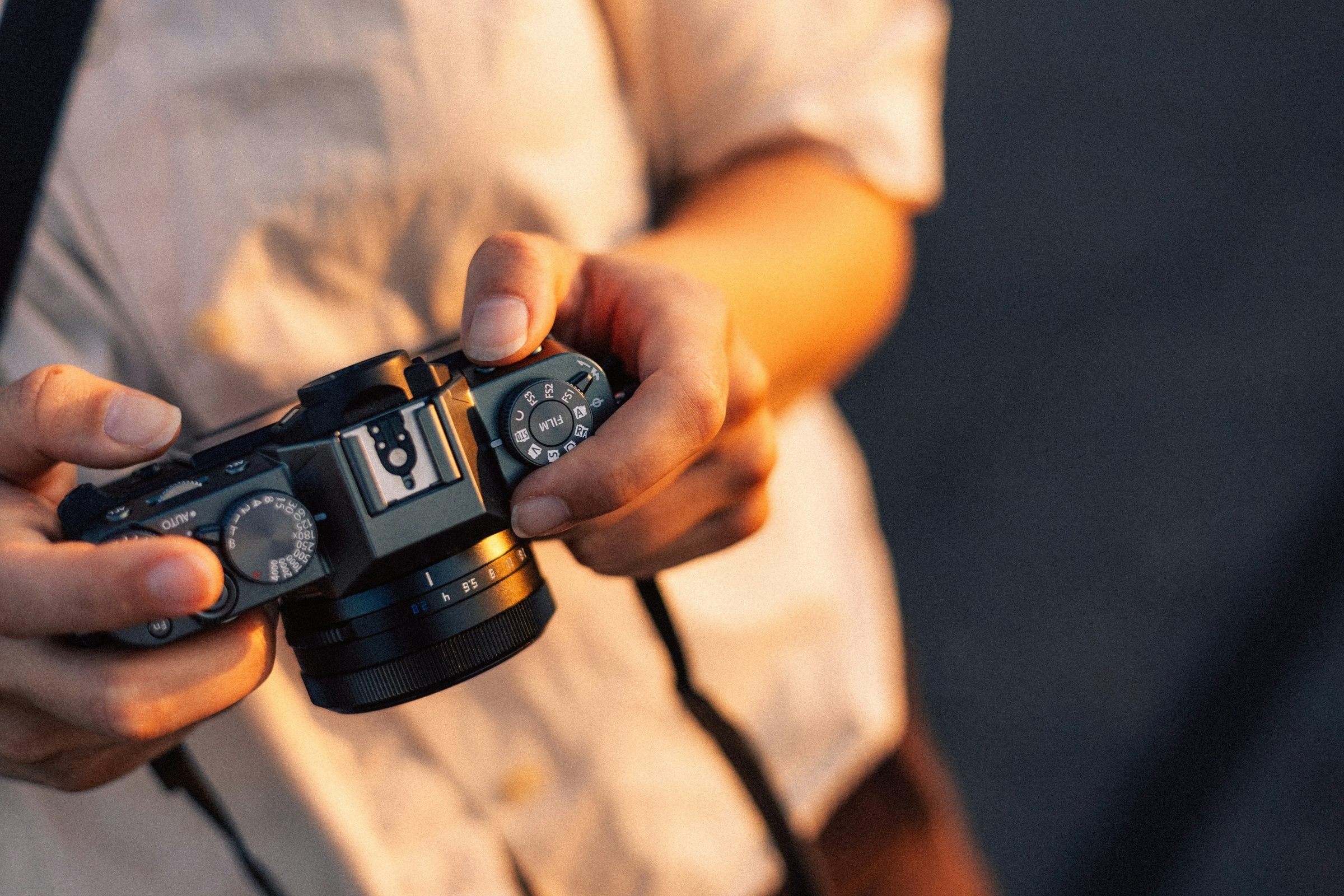 Hands holding a mirrorless camera in warm light