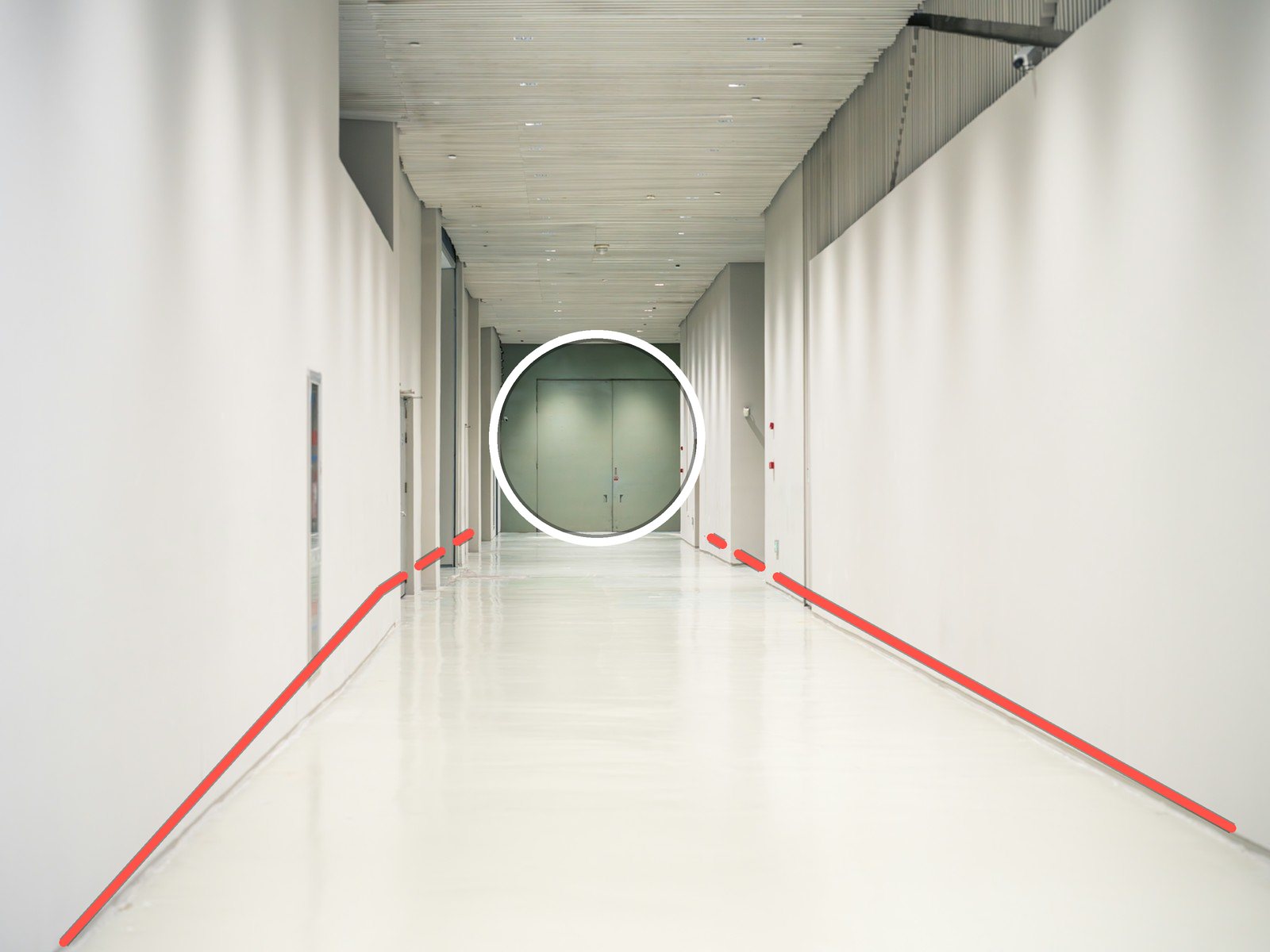 A long white hallway whose floor lines and walls lead to a green door at the far end