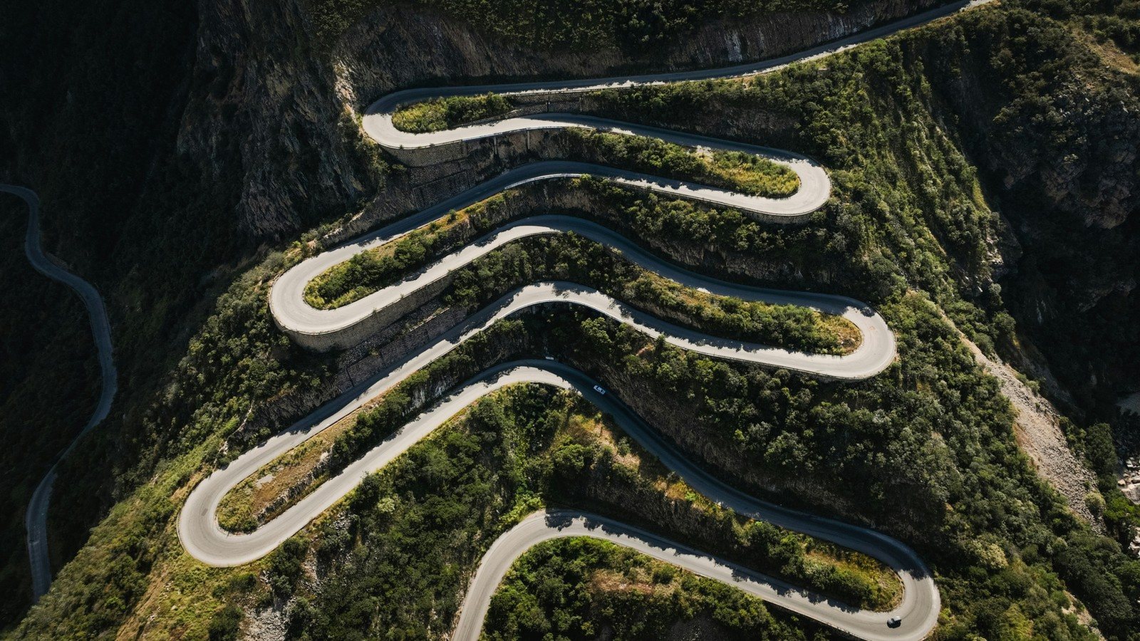 Aerial view of a mountain road zigzagging back and forth across a steep green slope