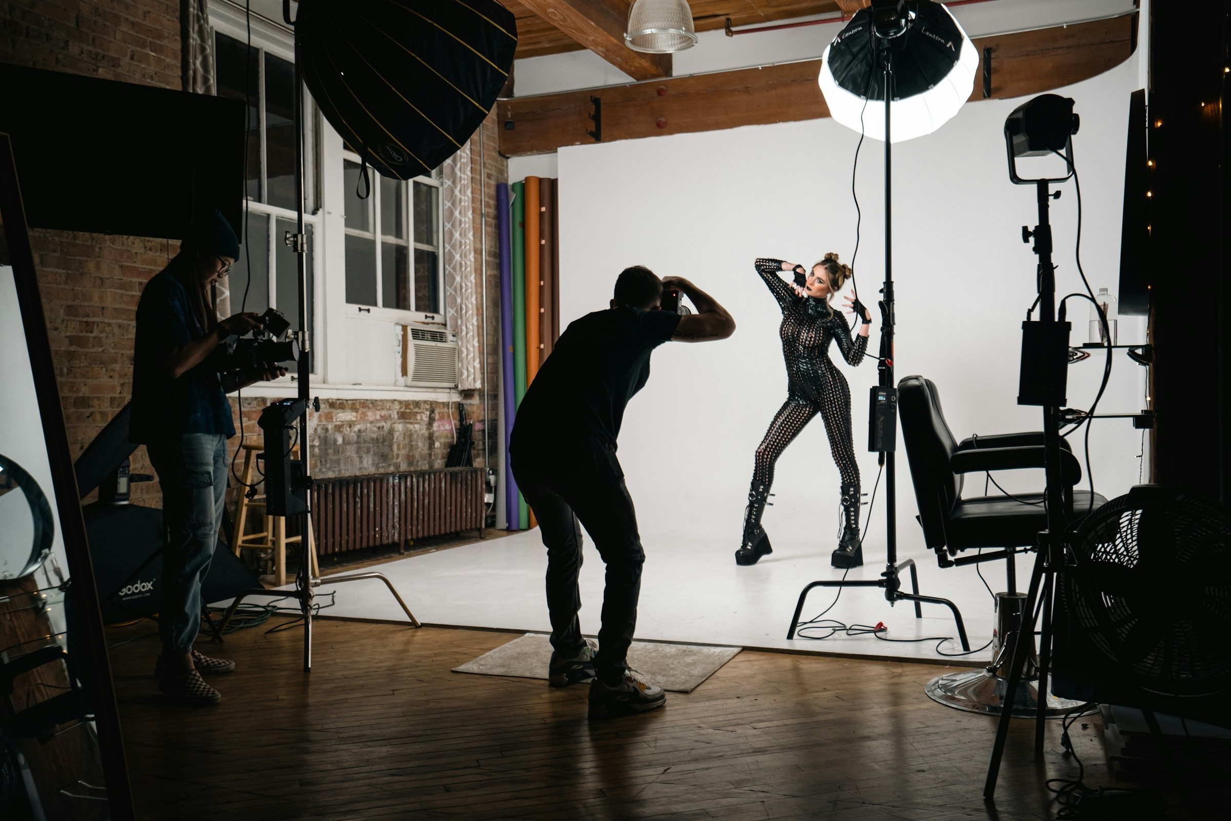 Photographer shooting a model on a white backdrop in a studio while an assistant films