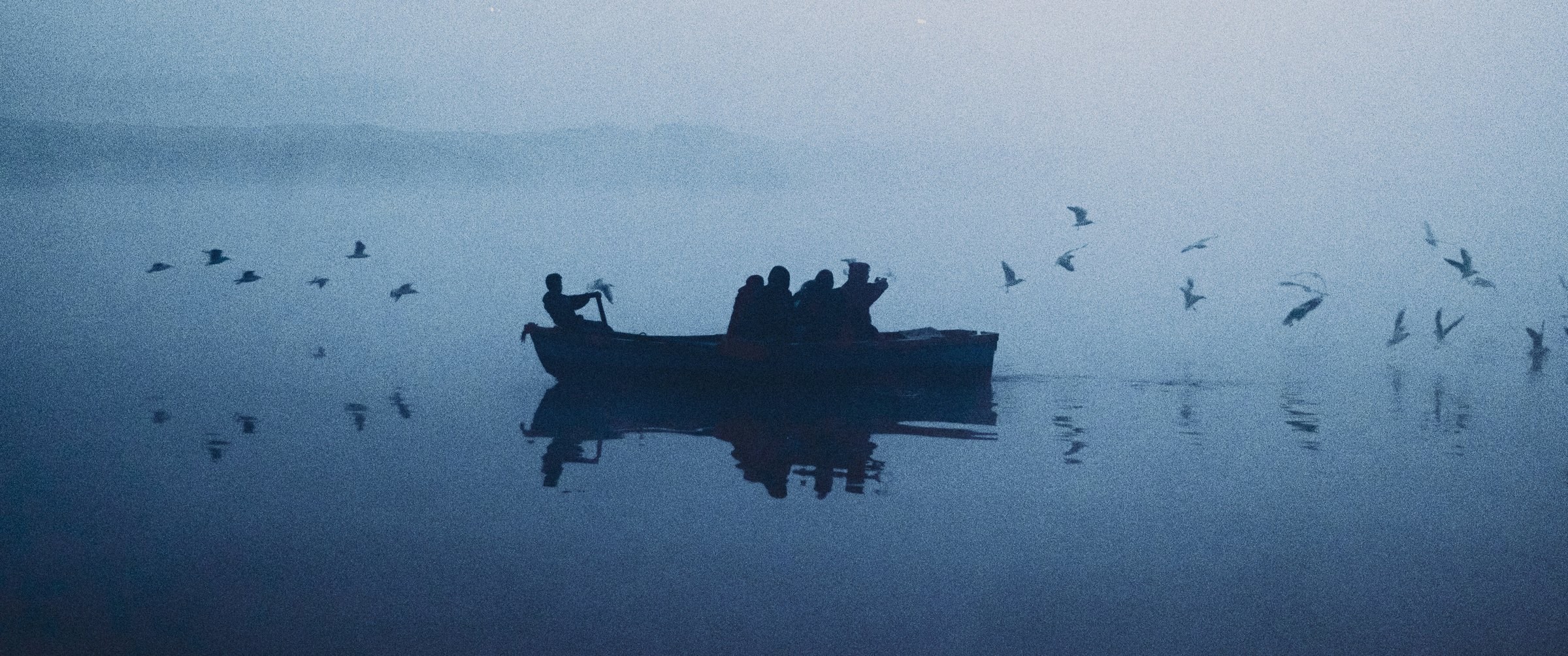 Rule of thirds in photography: a rowing boat and birds in morning fog on the Yamuna, the boat placed on the horizon line