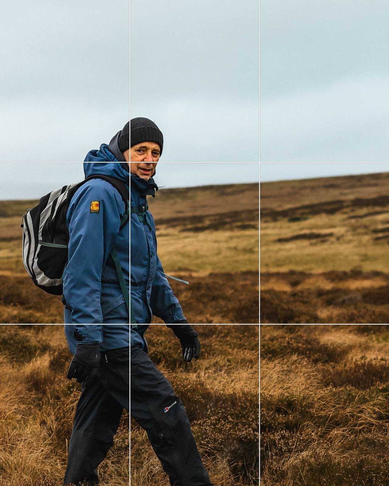 The same hiker cropped onto the left grid line with the open moorland ahead of him