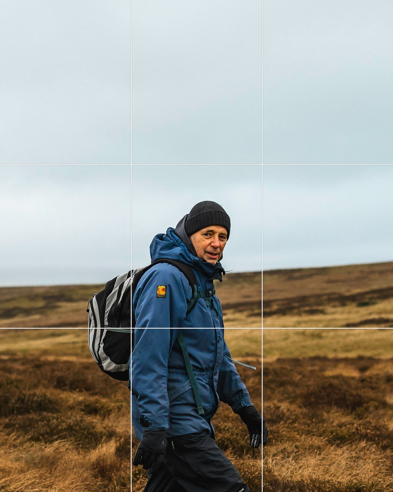 A hiker in a blue jacket centred in the frame on open moorland, grid overlaid